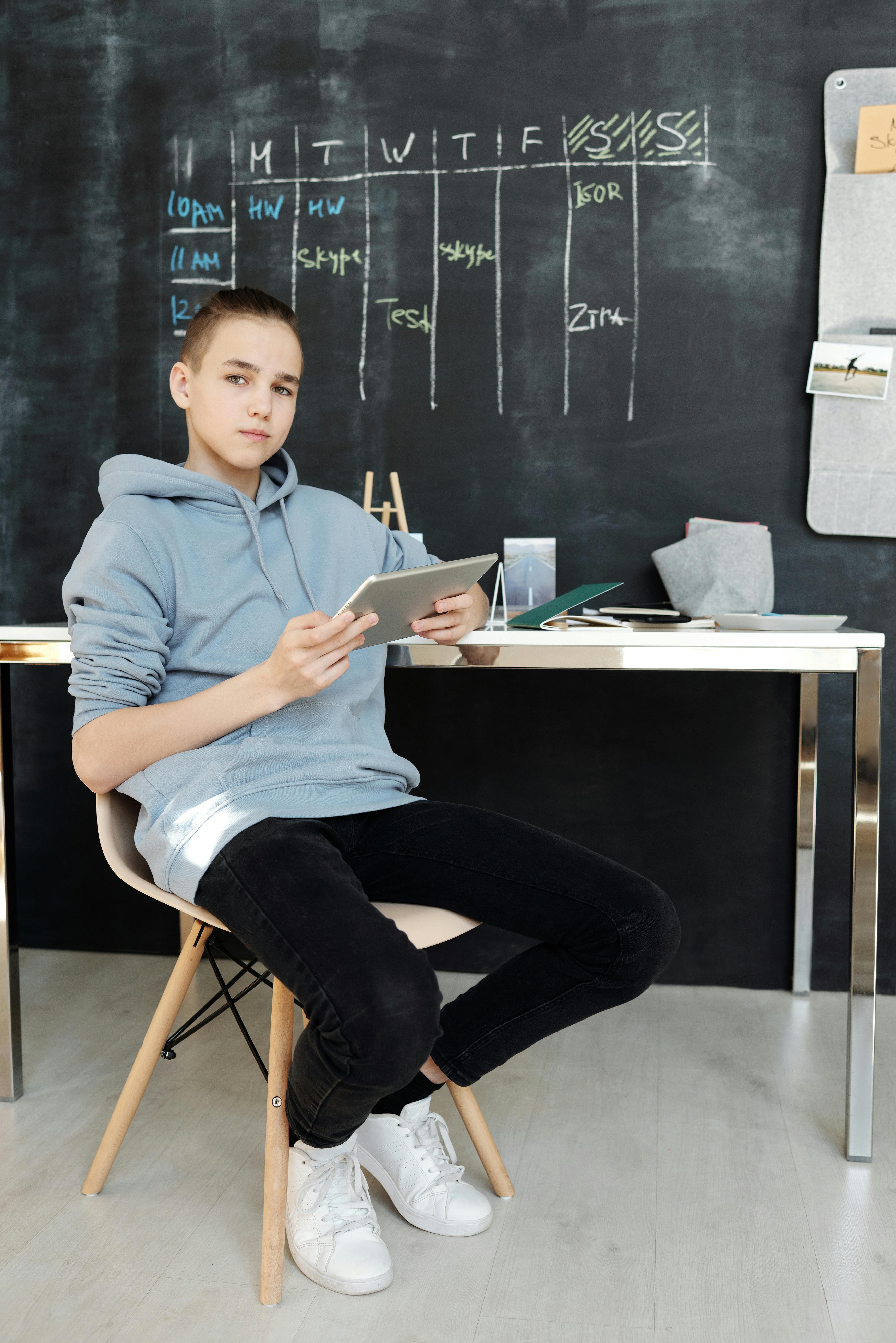 Schüler mit Tablet vor einem Wochenplan an der Tafel